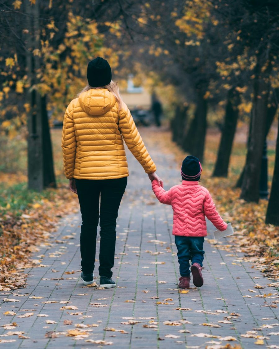 An adult and a child walking together on a tree-lined path